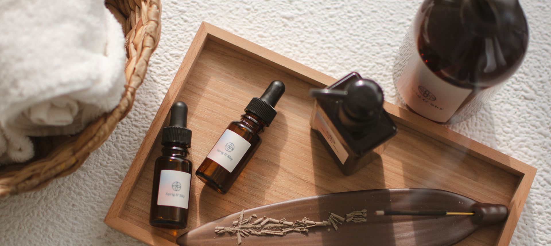 2 bottles of facial oil and serum displayed on a wooden tray next to a towel in a bowl