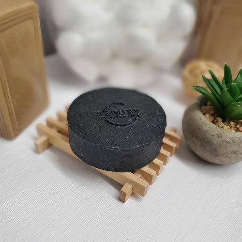 Activated Charcoal Soap  on a wood soap dish next to a plant