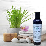 Blueberry Passion Body Wash in front of towels, soap, plant, candle and rocks